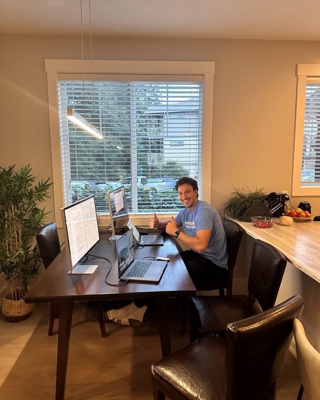 A teammate giving two thumbs up at a multi-monitor work session around Nathan’s dining table