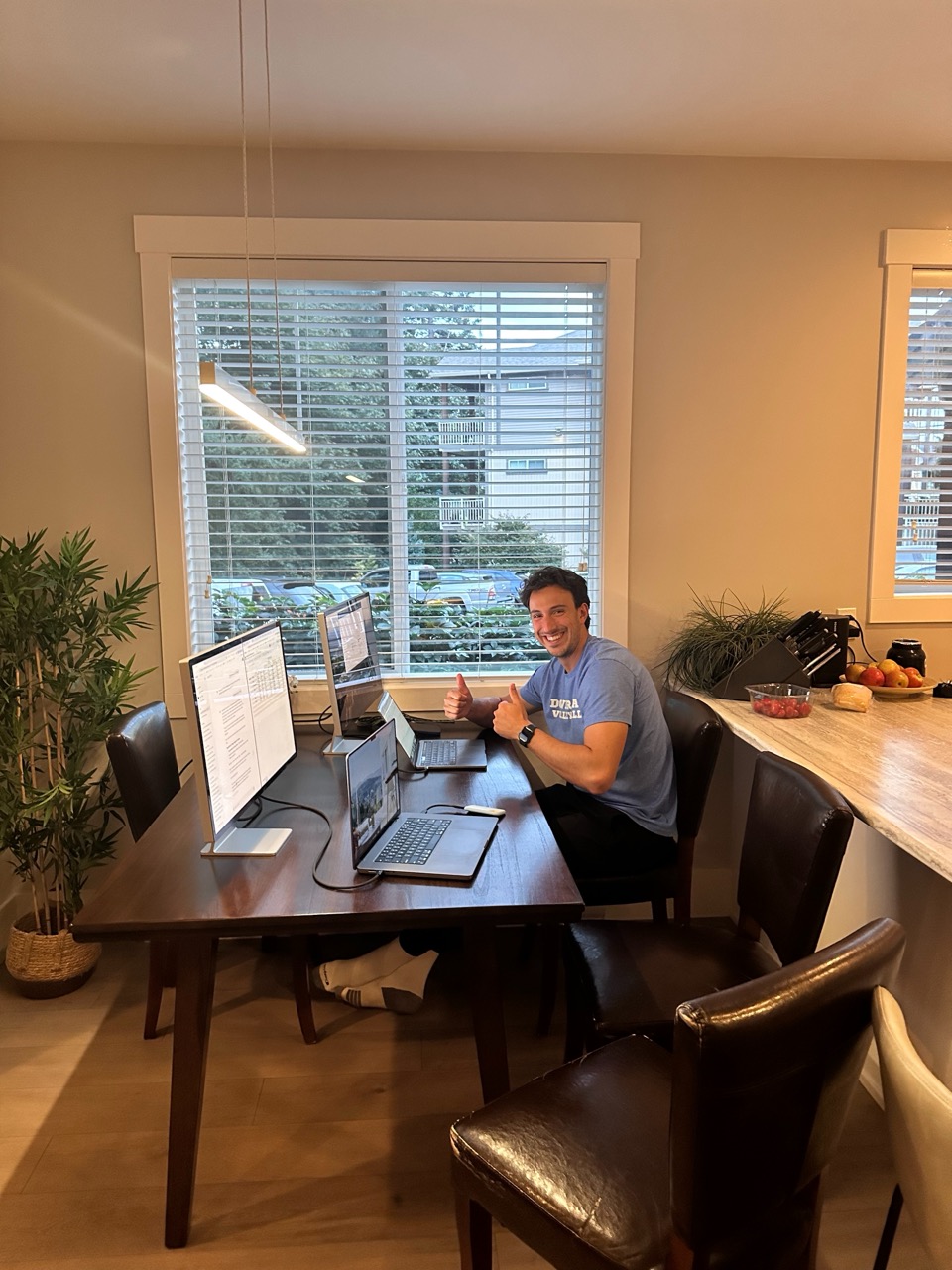 A teammate giving two thumbs up at a multi-monitor work session around Nathan&rsquo;s dining table